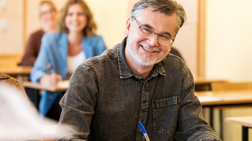 En smilende mann sitter og noterer